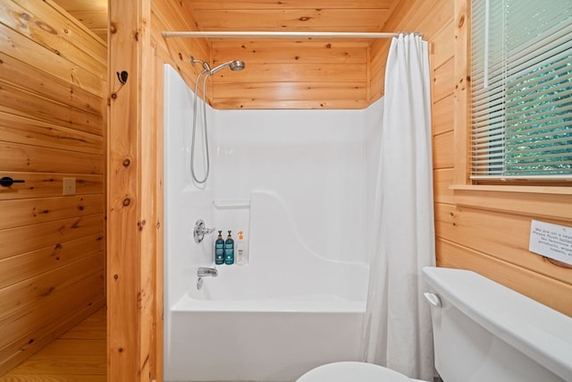 bathroom with wood walls, toilet, and shower / tub combo