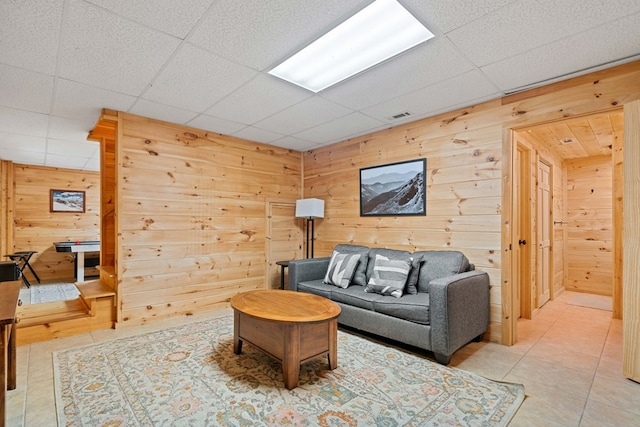 living room featuring tile patterned floors, a drop ceiling, and wood walls