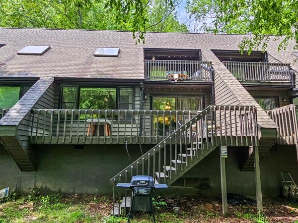 rear view of house featuring roof with shingles, stairs, and a balcony