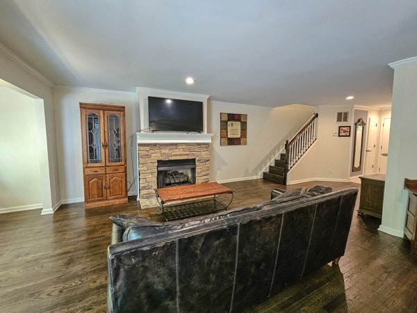 living area featuring stairway, ornamental molding, a fireplace, and dark wood-type flooring