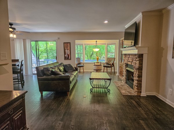 living room featuring ceiling fan, a stone fireplace, a wealth of natural light, and wood finished floors
