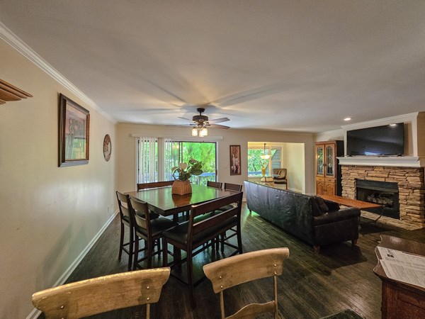dining room with crown molding, ceiling fan, a fireplace, baseboards, and wood finished floors