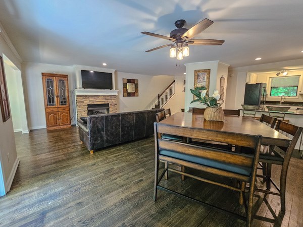 dining room with a ceiling fan, a fireplace, stairs, wood finished floors, and recessed lighting