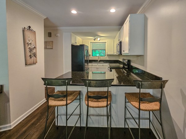 kitchen with crown molding, stainless steel appliances, dark wood-style floors, and a peninsula