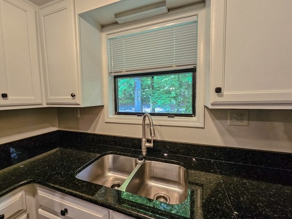 kitchen with a sink, white cabinets, and dark stone countertops