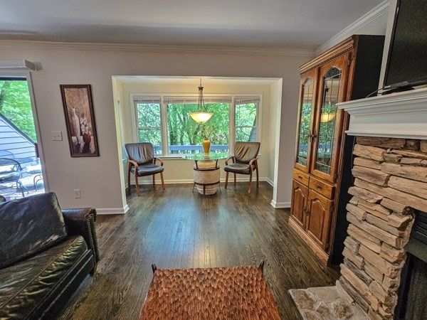 sitting room with a stone fireplace, ornamental molding, baseboards, and dark wood-style floors