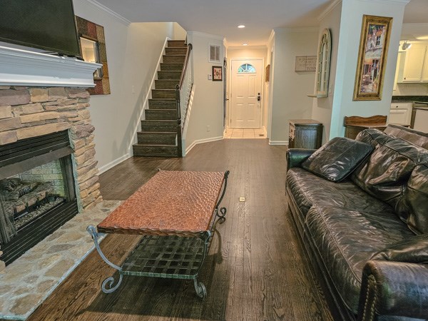 living room with crown molding, wood finished floors, a stone fireplace, stairway, and recessed lighting
