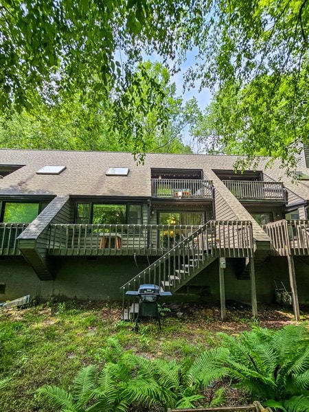 back of house featuring roof with shingles, stairway, and a deck