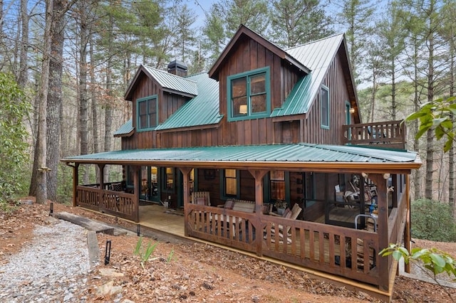 back of house with metal roof, board and batten siding, covered porch, and a chimney