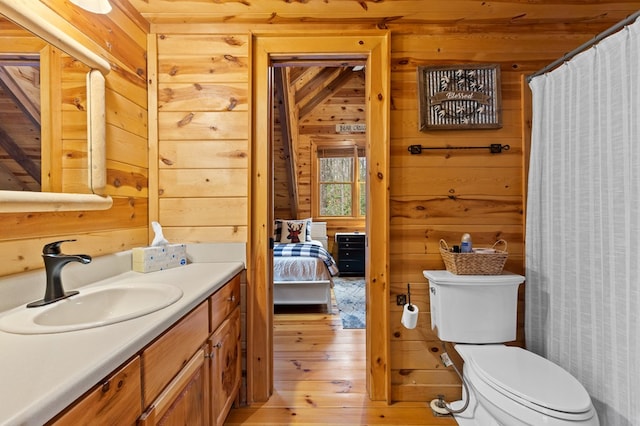 bathroom featuring wood-type flooring, wooden walls, vanity, and toilet