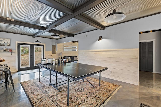 rec room featuring beam ceiling, french doors, wooden walls, concrete floors, and wainscoting