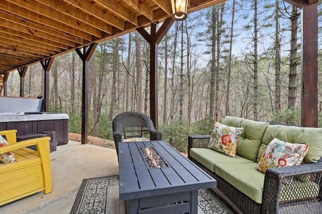 view of patio / terrace featuring a view of trees, an outdoor living space with a fire pit, and a hot tub