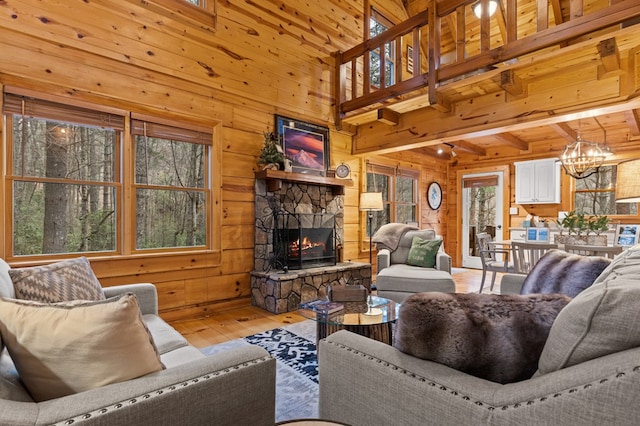 living room with wooden walls, an inviting chandelier, a stone fireplace, and light wood-style floors