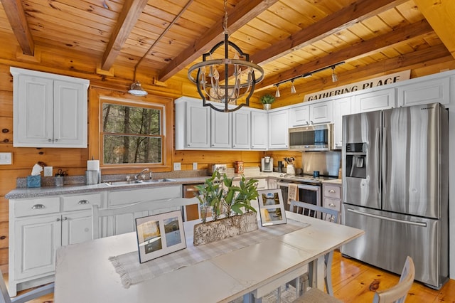 kitchen featuring a sink, wooden walls, appliances with stainless steel finishes, and white cabinets