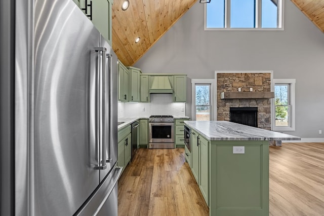 kitchen with appliances with stainless steel finishes, a healthy amount of sunlight, light wood-style floors, a fireplace, and green cabinets