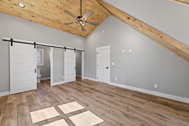 unfurnished bedroom featuring high vaulted ceiling, a barn door, wood finished floors, and baseboards