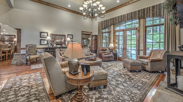 living area with a chandelier, light wood-type flooring, a towering ceiling, and crown molding