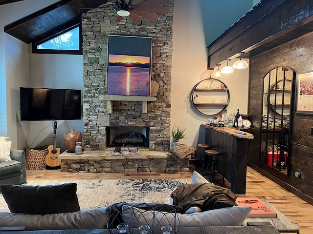 living room with wood-type flooring, a stone fireplace, beam ceiling, high vaulted ceiling, and ceiling fan