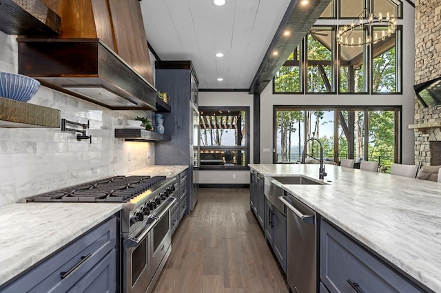 kitchen with stainless steel appliances, sink, light stone counters, a fireplace, and dark hardwood / wood-style flooring