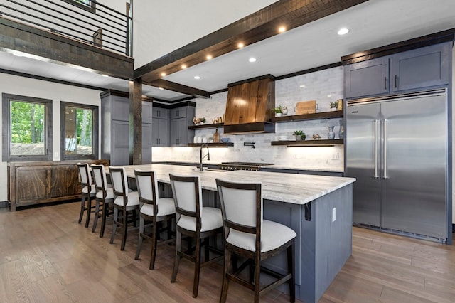 kitchen featuring a large island with sink, a breakfast bar area, light hardwood / wood-style flooring, built in fridge, and light stone countertops