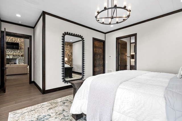 bedroom with ornamental molding, a chandelier, a stone fireplace, and wood-type flooring