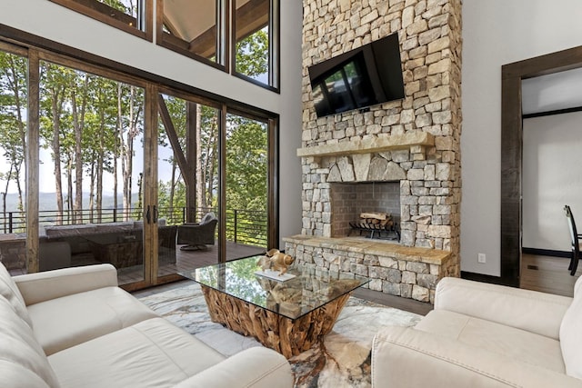 living room featuring a stone fireplace, light hardwood / wood-style flooring, and a high ceiling