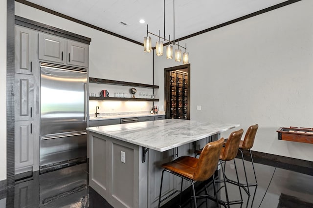 kitchen with a center island, built in fridge, decorative light fixtures, light stone counters, and ornamental molding