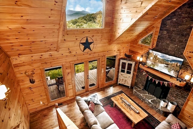 living room featuring wooden walls, high vaulted ceiling, wood-type flooring, a stone fireplace, and wooden ceiling