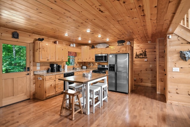 kitchen with stainless steel appliances, wooden walls, light brown cabinetry, and light hardwood / wood-style flooring