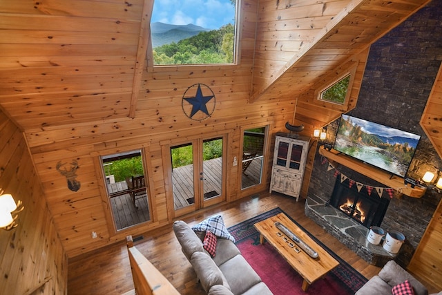 living room featuring a stone fireplace, hardwood / wood-style floors, high vaulted ceiling, wooden walls, and wood ceiling