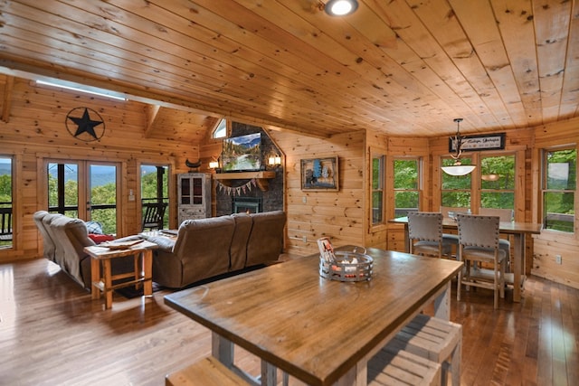 dining room with wood ceiling, vaulted ceiling, wooden walls, a fireplace, and hardwood / wood-style floors