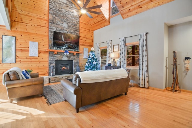 living area featuring high vaulted ceiling, ceiling fan, hardwood / wood-style flooring, a stone fireplace, and baseboards