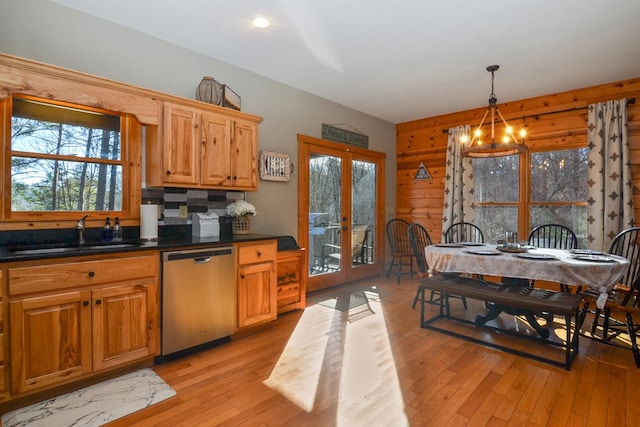 kitchen with stainless steel dishwasher, a sink, french doors, light wood finished floors, and dark countertops