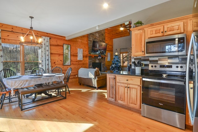 kitchen featuring stainless steel appliances, vaulted ceiling, light wood-style flooring, wooden walls, and a stone fireplace