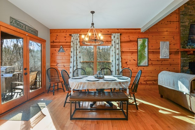 dining space with french doors, light wood finished floors, and wood walls