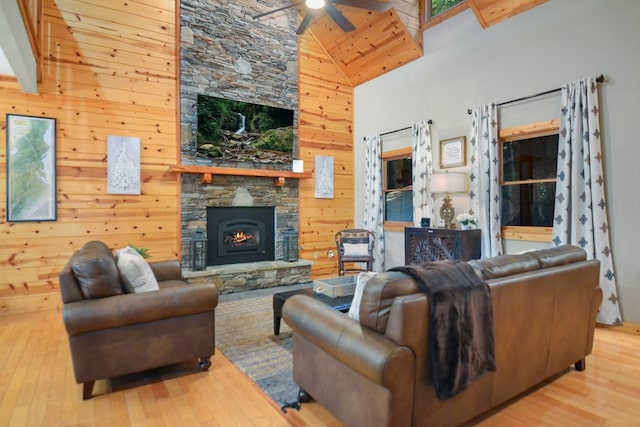living area with a fireplace, a ceiling fan, high vaulted ceiling, wood finished floors, and wood walls