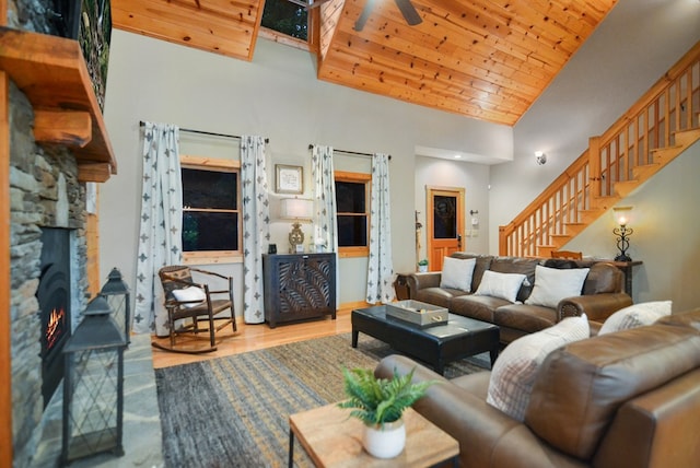 living room with a stone fireplace, stairway, wood finished floors, ceiling fan, and high vaulted ceiling