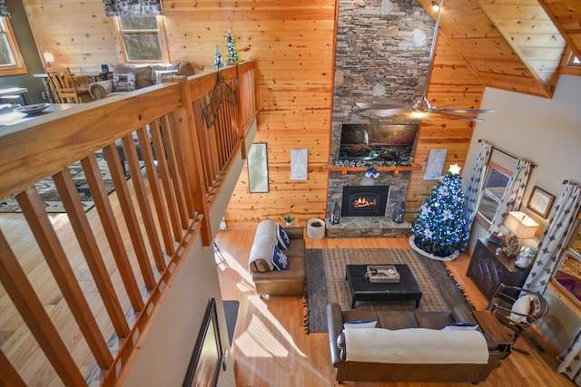 living area featuring wood finished floors, wooden walls, a stone fireplace, high vaulted ceiling, and ceiling fan