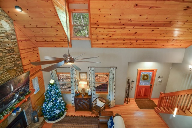 living area with wood finished floors, a ceiling fan, lofted ceiling, and a stone fireplace