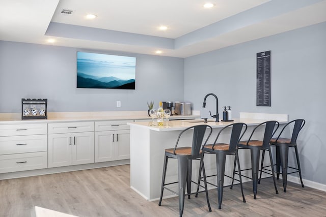 bar featuring a sink, light wood-type flooring, baseboards, a raised ceiling, and recessed lighting