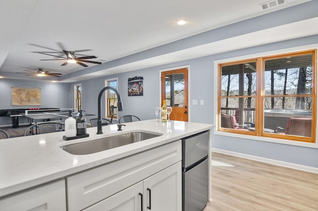 kitchen with a sink, white cabinets, light wood-style floors, ceiling fan, and baseboards