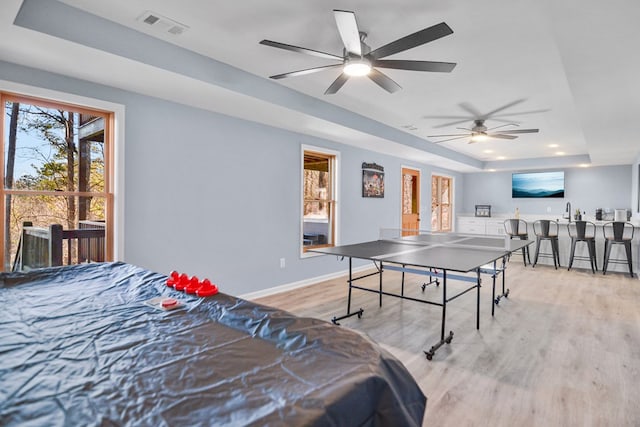 playroom with a tray ceiling, light wood-style floors, a ceiling fan, baseboards, and bar area