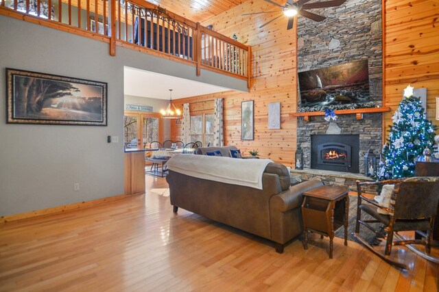 living area featuring a ceiling fan, baseboards, a stone fireplace, wood finished floors, and a towering ceiling