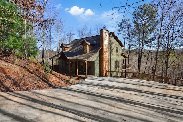 view of side of property with driveway, covered porch, and a chimney