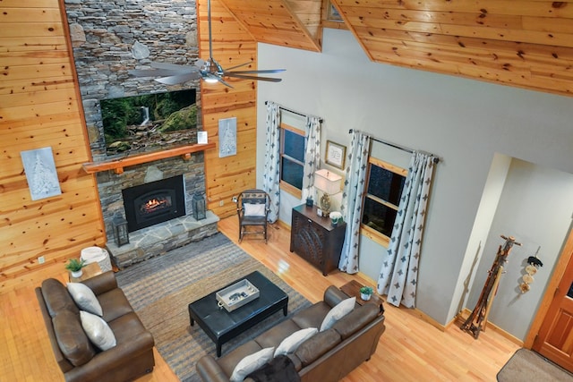 living room with lofted ceiling, wood finished floors, ceiling fan, a stone fireplace, and wooden ceiling