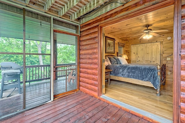 bedroom featuring access to exterior, rustic walls, ceiling fan, multiple windows, and hardwood / wood-style floors