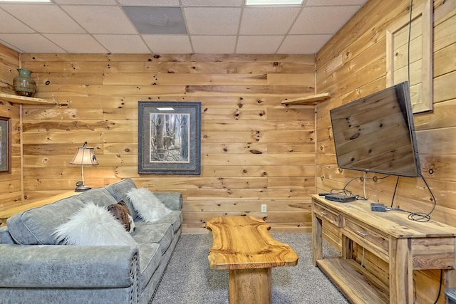 living room featuring carpet, a paneled ceiling, and wooden walls