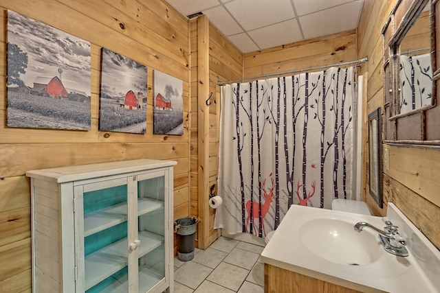 bathroom with tile patterned flooring, vanity, a paneled ceiling, and wooden walls