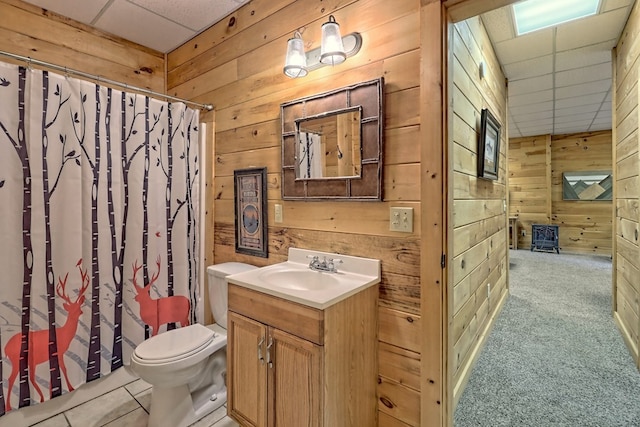 bathroom with a drop ceiling, wood walls, toilet, vanity, and a shower with shower curtain