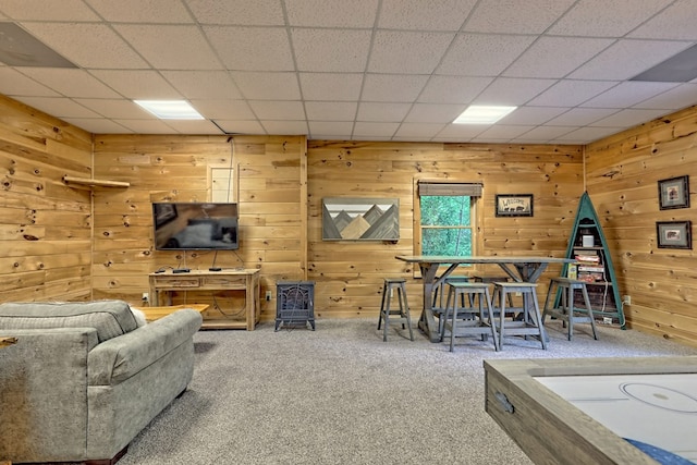 living room with a paneled ceiling, wood walls, and carpet floors